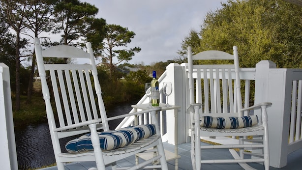 Two white rocking chairs with striped cushions on a wooden deck by a body of water. - 
Cozy Waterfront Beach House with Private Beach/Pier/Tennis Courts (Pensacola)