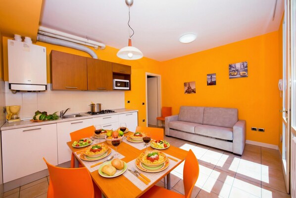 A bright orange living room with a sofa and a dining area with a table set for a meal.