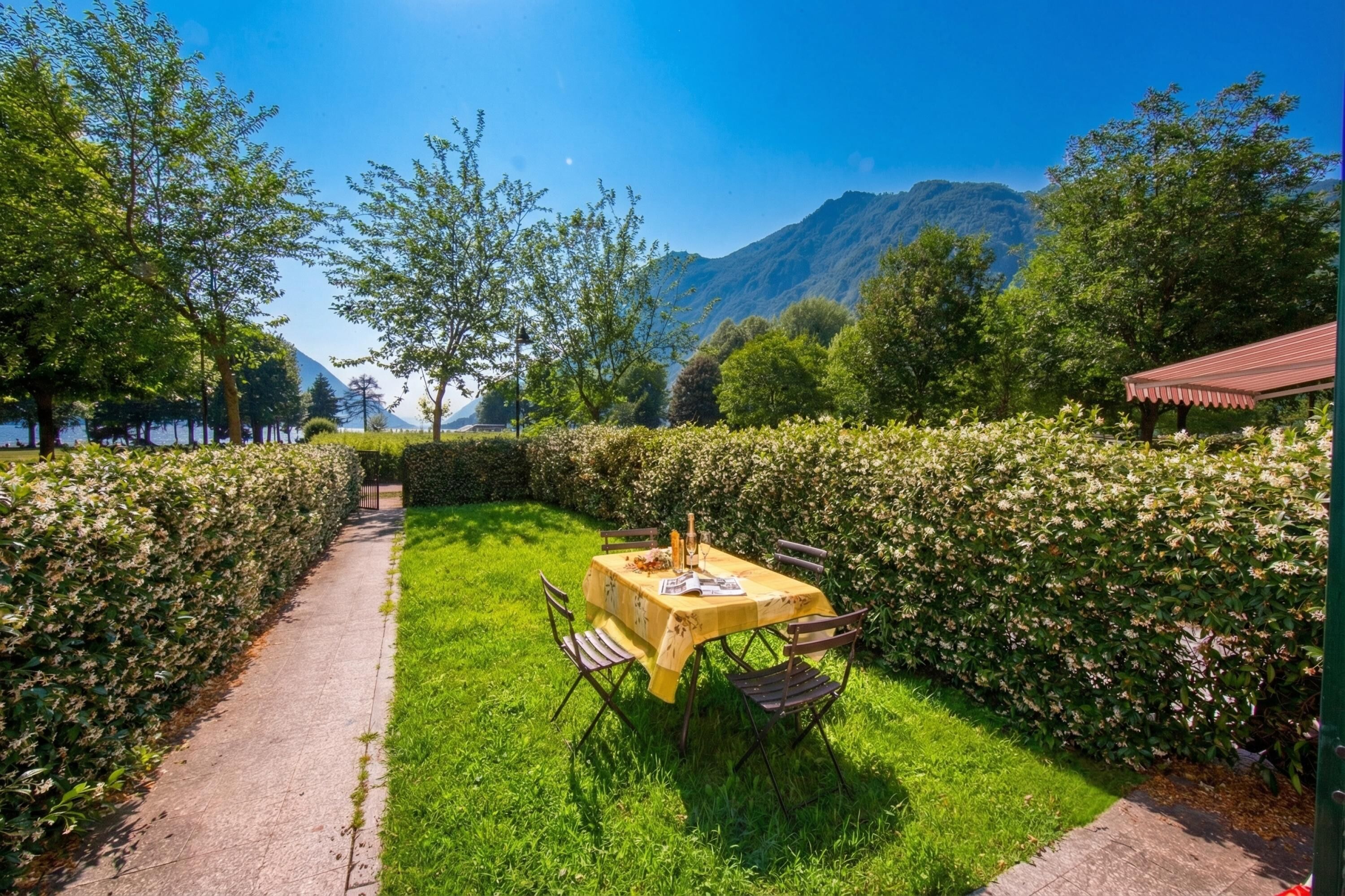 Une table dressée à l’extérieur, avec des chaises, entourée d’une haie et avec une montagne en arrière-plan.