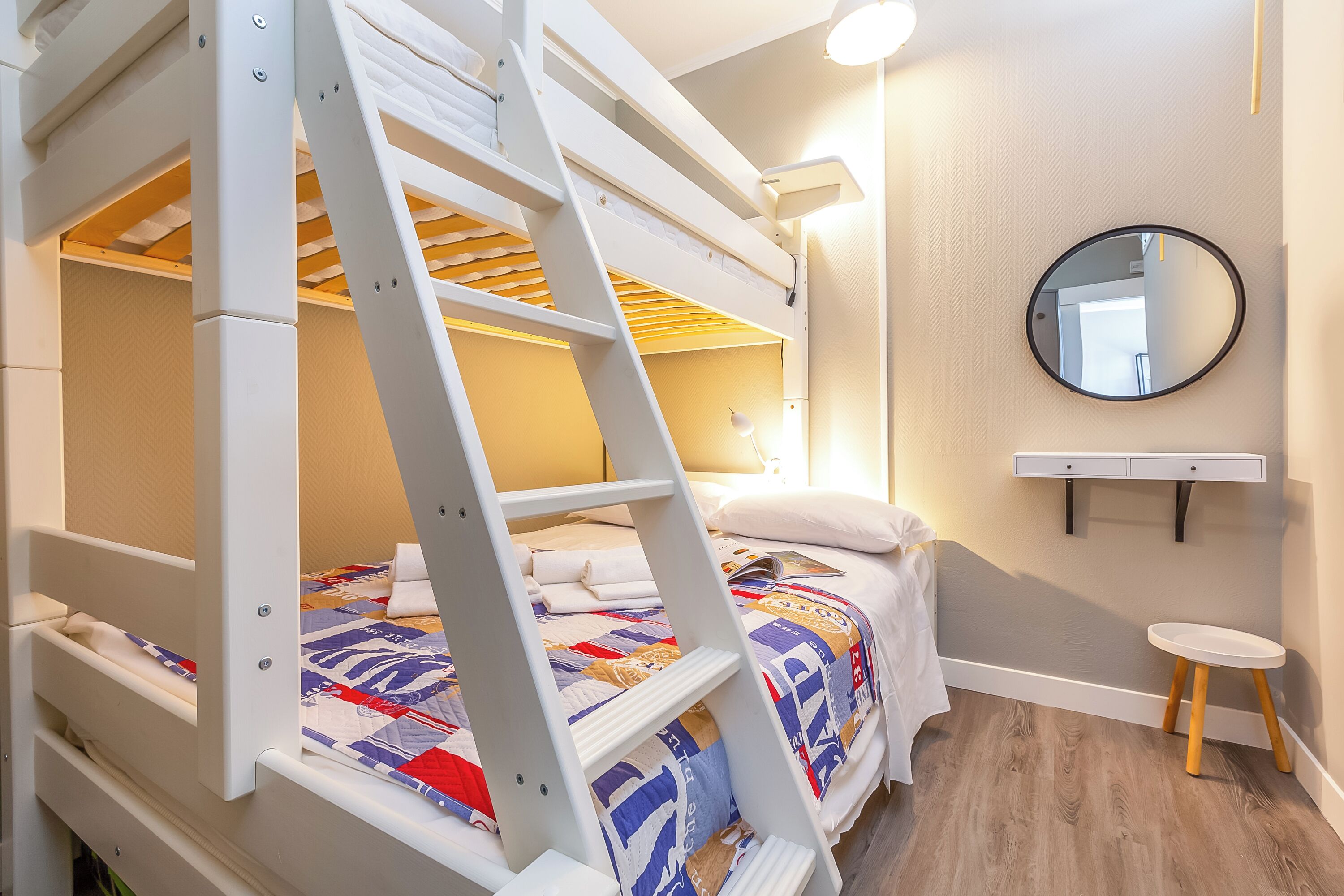 Une chambre avec un lit superposé, une échelle, une table de chevet, un miroir et un petit tabouret.