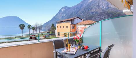 A balcony with a table set for two, overlooking a mountainous landscape and a body of water.
