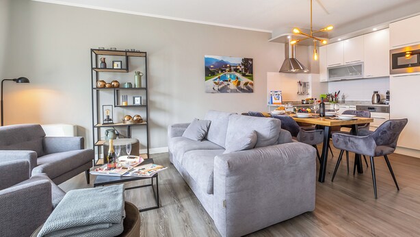 A modern living room with a grey sofa, a coffee table with magazines, and a dining area with a wooden table and chairs. - Porto Letizia P8, Porlezza, Italy (Porlezza)