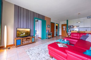 Ett modernt vardagsrum med en röd soffa, en tv och ett köksområde i bakgrunden.