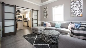 A modern living room with a sectional sofa, ottoman, and a kitchen in the background. - Beautiful City View GEM of NOLA, Vacation Luxury! (New Orleans)