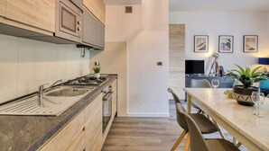 A modern kitchen with a built-in oven, a stainless steel sink, and a dining area with a marble table and chairs. - Porto Letizia Orchidea 2, Porlezza, Italy (Porlezza)