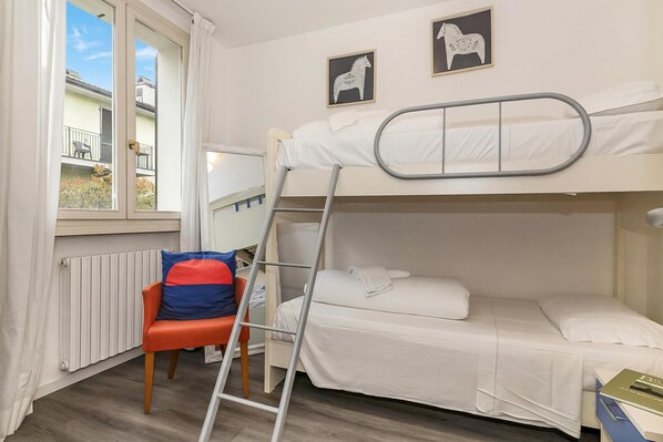 A bunk bed room with a ladder, a chair, a radiator, and two framed pictures on the wall.