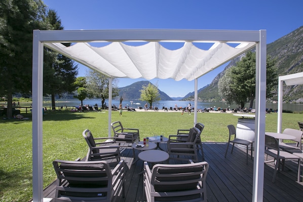 A wooden deck with outdoor seating and a white canopy overlooking a lake and mountains.
