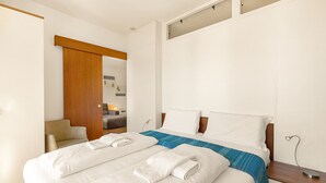 A hotel room with a large bed, a wooden door, a chair, and a small table with a lamp. - Porto Letizia S5, Porlezza, Italy (Porlezza)