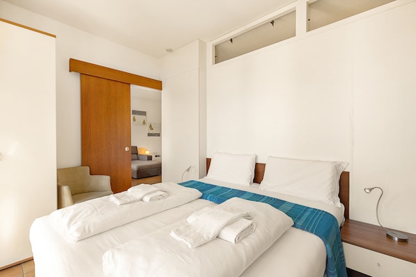 Habitación de hotel con una cama grande, una puerta de madera, una silla y una mesita con lámpara.
