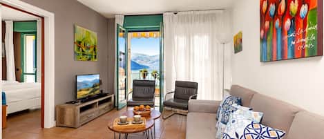 A living room with a television, a sofa, a coffee table, and a view of a lake through an open door.