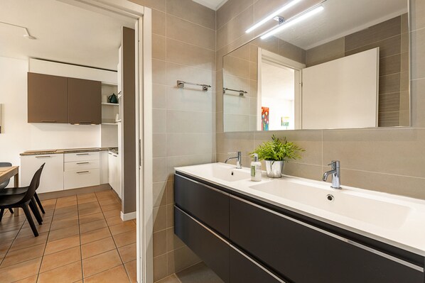 A modern bathroom with a large mirror, two sinks, and a potted plant.