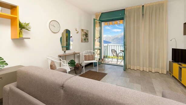 En moderne stue med sofa, stole, et lille bord og et TV-møbel. Der er en balkon med udsigt til bjergene.