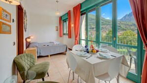 A room with a bed, a dining table set for two, and a view of a mountainous landscape through large windows.