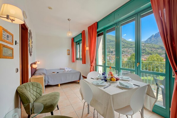 Une chambre avec un lit, une table à manger dressée pour deux personnes et une vue sur un paysage montagneux, visible à travers de grandes fenêtres.
