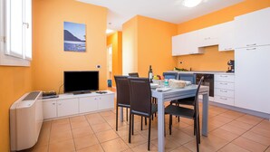 A compact kitchen with white cabinets, a dining table with chairs, a flat-screen TV, and a small refrigerator. - Porto Letizia Deluxe, Porlezza, Italy (Porlezza)