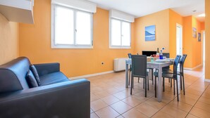 A modern living room with a sofa, dining table, chairs, and a kitchen area with a stove. - Porto Letizia Deluxe, Porlezza, Italy (Porlezza)