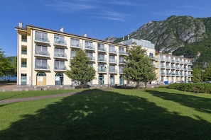 Ein mehrstöckiges Hotel mit Balkonen, einem Berg im Hintergrund und einem gepflegten Rasen.