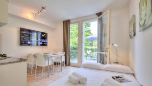 A hotel room with a bed, a desk, a TV, and a balcony with a table and chairs. - Porto Letizia Ortensia 3, Porlezza, Italy (Porlezza)