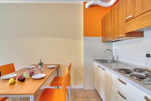A modern kitchen with white cabinets, a stainless steel stove, and a dining area with orange chairs and a wooden table set for four.