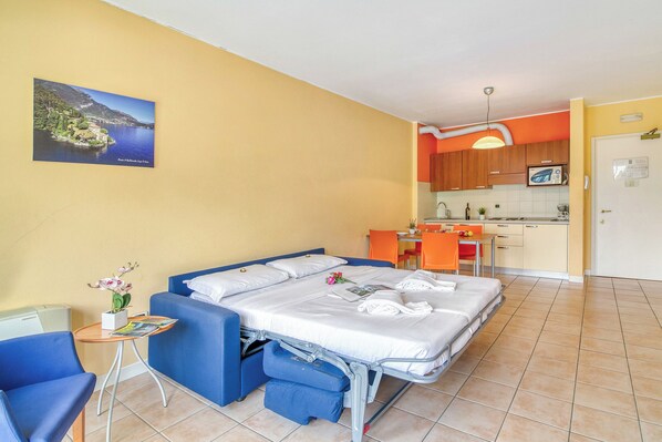 A hotel room with a bed, a small table with a vase of flowers, and a view of the kitchen and dining area. - Porto Letizia T17, Porlezza, Italy (Porlezza)