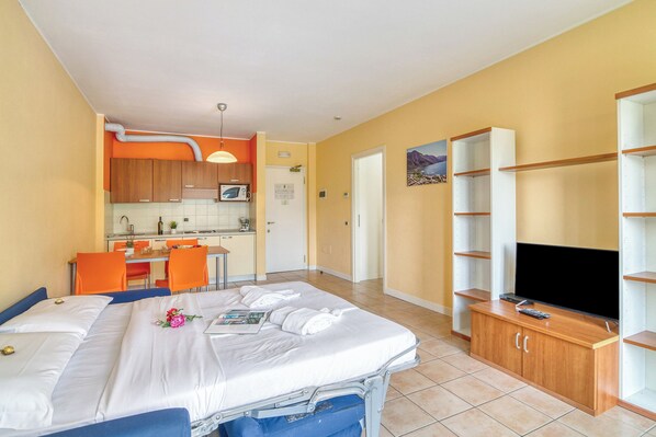A hotel room with a bed, a TV, a kitchen area, and a dining table.