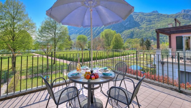 A balcony with a table set for dining, a large umbrella, and a scenic mountain view.