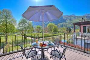 Varanda com mesa posta para refeições, um grande guarda-sol e uma vista panorâmica das montanhas.