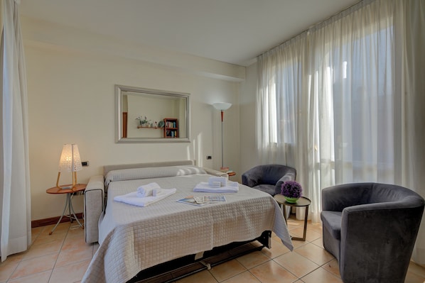 A hotel room with a bed, a chair, a lamp, a mirror, and a view of the outside. - Porto Letizia Ortensia 6, Porlezza, Italy (Porlezza)