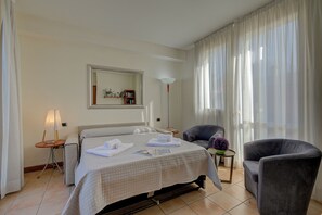 A hotel room with a bed, a chair, a lamp, a mirror, and a view of the outside.