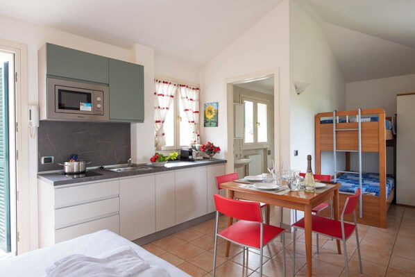 A compact kitchen with a microwave, sink, and a dining area with red chairs. - Porto Letizia Mimosa 5, Porlezza, Italy (Porlezza)