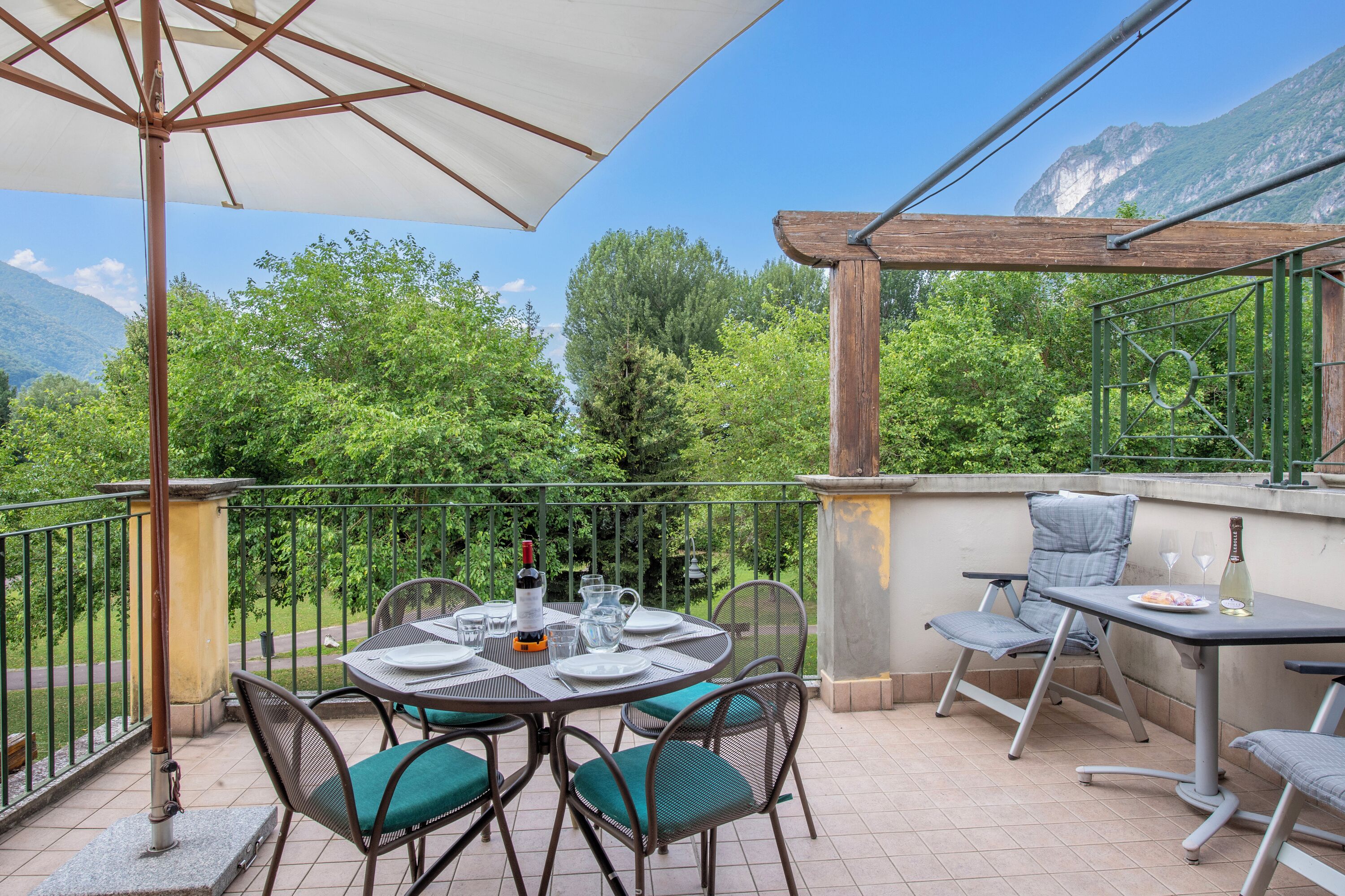 A terrace with a table set for dining, chairs, and a pergola providing shade.