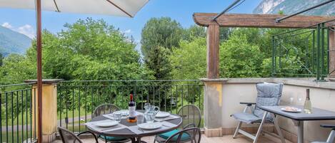A terrace with a table set for dining, chairs, and a pergola providing shade.