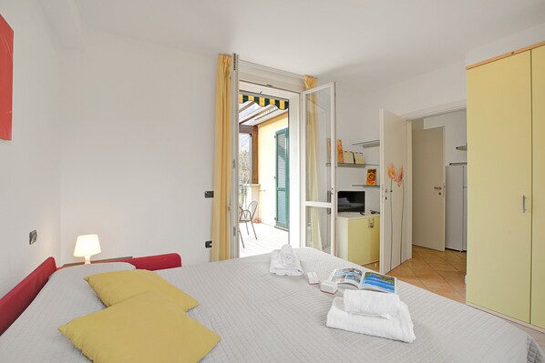A hotel room with a bed, a bedside table with a lamp, a wardrobe, and an open door leading to a balcony. - Porto Letizia Tulipano 5, Porlezza, Italy (Porlezza)