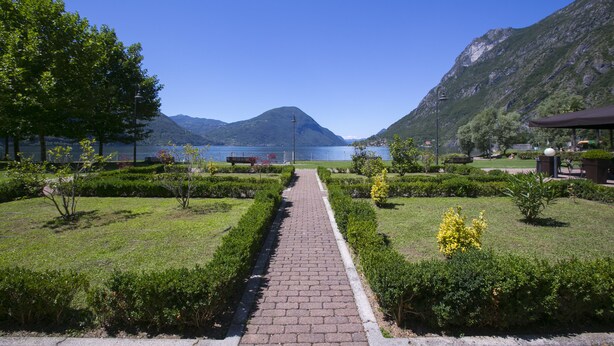 Ein gepflasterter Weg führt zu einem See, im Hintergrund Berge.