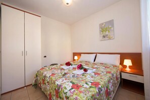 Een slaapkamer met een bed, nachtlampjes, een nachtkastje, een kledingkast en een schilderij aan de muur.