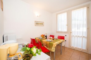 A dining area with a table set for two, a window with curtains, and a wall-mounted picture. - Porto Letizia Dalia 3, Porlezza, Italy (Porlezza)