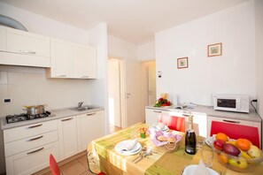 A compact kitchen with white cabinets, a gas stove, a microwave, and a dining area with a table set for two. - Porto Letizia Dalia 3, Porlezza, Italy (Porlezza)