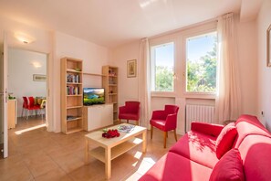 A living room with a sofa, two red chairs, a coffee table with red roses, a TV on a wooden stand, and bookshelves. - Porto Letizia Dalia 3, Porlezza, Italy (Porlezza)