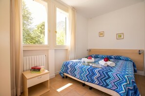 Ein Hotelzimmer mit Bett, Nachttisch, einem Fenster mit Vorhängen und einer Heizung.