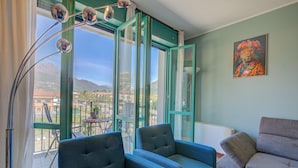 A room with two blue armchairs, a grey sofa, a large window with a view of mountains, and a painting of a leopard.
