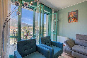 A room with two blue armchairs, a grey sofa, a large window with a view of mountains, and a painting of a leopard.