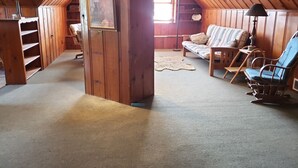 Een gezellig zolderkamer met houten wanden, een lijst met foto, een bank, een schommelstoel en een lamp.