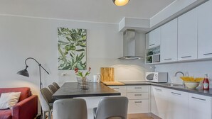 Une cuisine moderne avec des meubles blancs, une table à manger avec des chaises, un canapé rouge et un tableau accroché au mur.