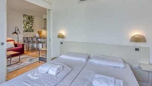 Une chambre d’hôtel avec deux lits, un canapé rouge, un coin repas et une cuisine à l’arrière-plan.