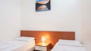 Una camera d'albergo con due letti singoli, una testata del letto in legno, un comodino con una lampada e un quadro raffigurante un paesaggio sulla parete.