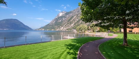 A park with a paved path, a lake, and mountains in the background.