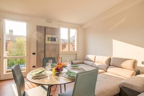 Un coin repas avec une table ronde dressée pour quatre personnes, un canapé et une vue sur l’extérieur.