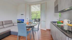 A modern kitchen with a dining area, a sofa, and a view of greenery through an open door. - Porto Letizia Iris 3, Porlezza, Italy (Porlezza)