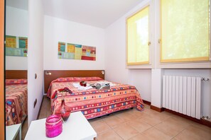 A bedroom with two beds, a white table, a pink vase, and a window with blinds.