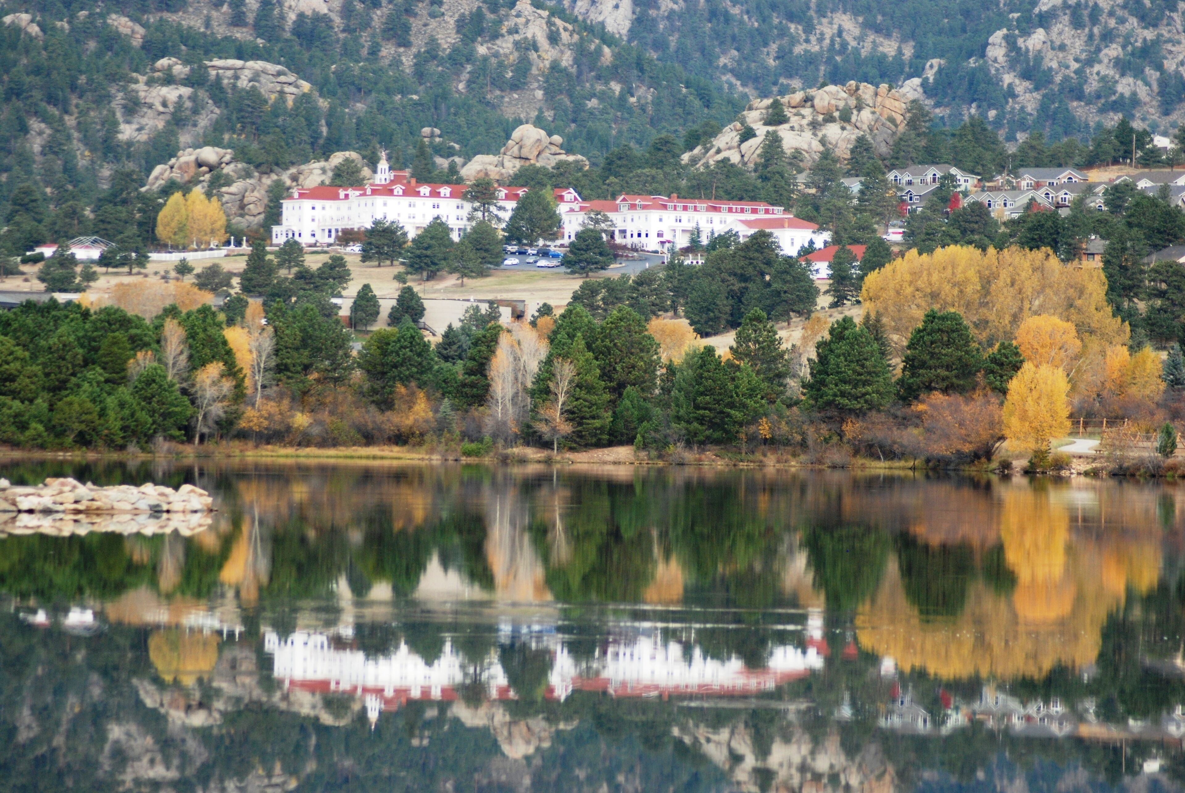A large building with a red roof, surrounded by trees and a lake.